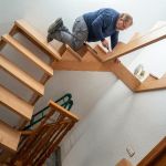 Un carpintero instalando una escalera de madera en una vivienda, trabajando con precisión sobre la estructura de los peldaños mientras utiliza herramientas manuales para el ajuste de las piezas.