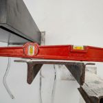 Primer plano de un nivel de burbuja rojo colocado sobre una estructura metálica durante la medición profesional de una escalera, garantizando la nivelación y precisión técnica en el proceso de montaje.